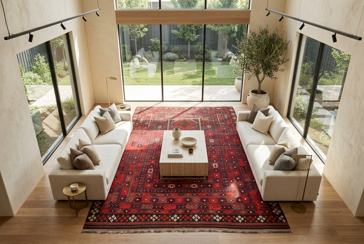 Oversized red and black Afghan Kilim rug styled in a luxury open-plan living room with cream sofas, travertine coffee table and natural oak flooring.